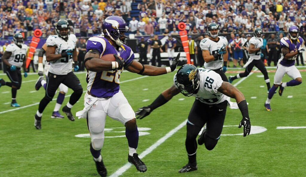 Adrian Peterson, in a purple Vikings uniform, stiff-arms a Jacksonville Jaguars defender during the 2012 season opener